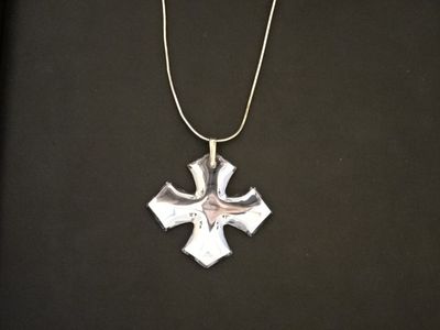 un gros plan d'un pendentif en forme de croix suspendu à une chaîne, posé sur une surface noire