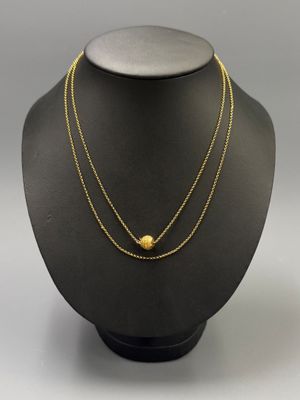a gold necklace with a ball and chain on a mannequin