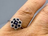 la main d'une femme portant une bague ornée d'une fleur en diamants et saphirs