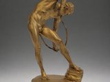 bronze statue of a man bending over on a marble base