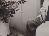 a black and white photo of a man sitting next to a potted plant