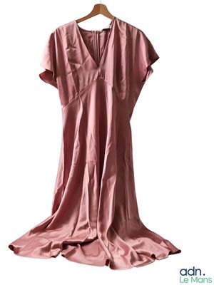 La robe rose est suspendue à un cintre sur un fond blanc.