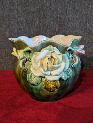 un vase vert orné d'une rose blanche, posé sur un tissu rouge