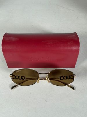 des lunettes de soleil et leur étui posés sur une surface blanche, avec une boîte rouge