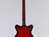 a red electric guitar hanging from a string on a white wall