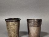 two silver cups with designs on them on a gray background