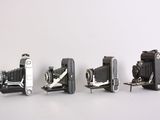 several old cameras are lined up in a row on a white surface