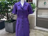 une robe violette posée sur un mannequin devant un immeuble