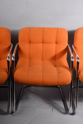 trois chaises orange placées les unes à côté des autres contre un mur blanc