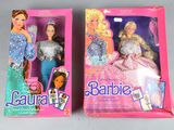 two barbie dolls are in a pink box on a gray surface