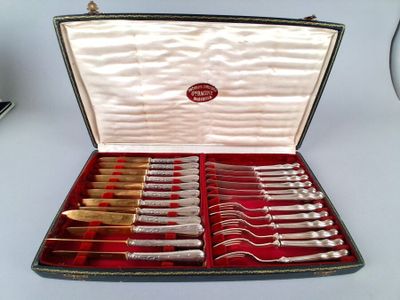 des couverts rangés dans un coffret posé sur une table blanche recouverte d'une nappe rouge