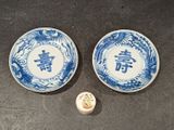 two blue and white plates with chinese writing on them next to a small container