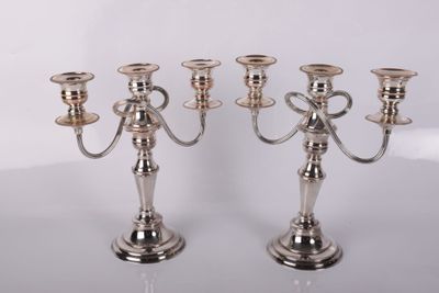 trois bougeoirs en argent posés sur une table, sur fond blanc
