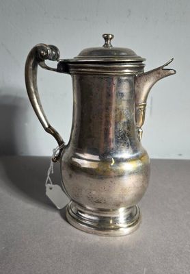 une cafetière ancienne en argent avec son couvercle, posée sur une table