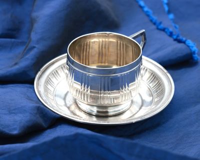 a silver cup and saucer sitting on a blue cloth