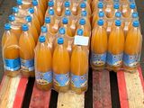 Plusieurs bouteilles de jus d'orange sont posées sur une palette devant une pile de palettes en bois