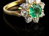 une bague ovale sertie d'une émeraude et d'un groupe de diamants, posée sur un fond noir