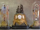 trois horloges différentes, posées sur une table sous des dômes en verre