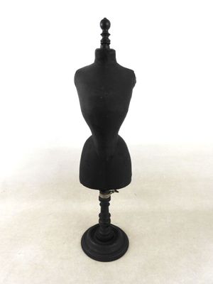 un mannequin noir posé sur un socle noir, devant un fond blanc