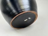 a black vase with a brown rim sitting on a table