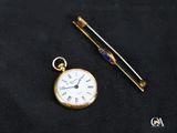 une montre de poche en or et une aiguille posée sur un tissu noir