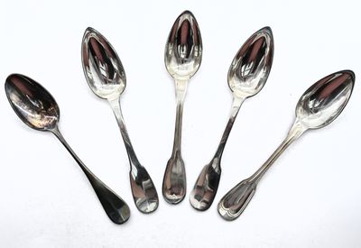 six cuillères en argent sont alignées sur une surface blanche