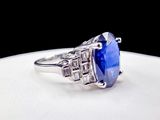 a close up of a blue sapphire and diamond ring on a white plate