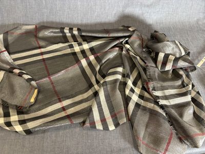 une écharpe à carreaux Burbers posée sur un canapé gris, recouverte d'une couverture à carreaux noirs et blancs