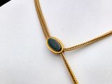 a gold necklace with a green stone on a mannequin neck