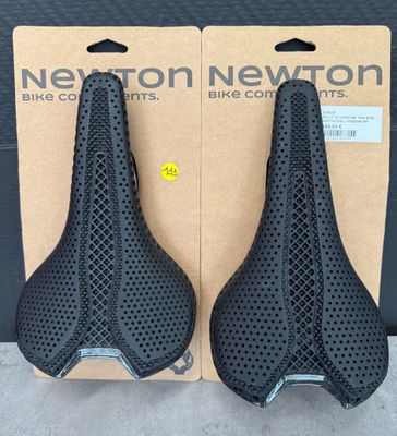 deux selles noires percées de trous, dans une boîte en carton