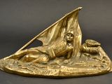 bronze statue of a man laying on a rock with a sailboat