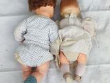 a baby doll laying on a white sheet with a pair of socks