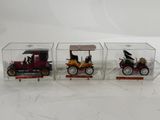 trois modèles réduits de voitures sont exposés dans une vitrine posée sur une surface blanche
