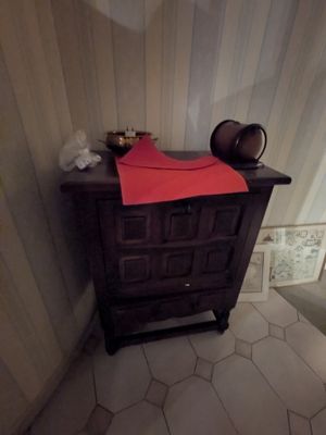 une petite armoire dans un coin de la salle de bains, sur laquelle est posée une serviette rouge