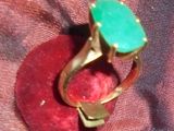 une bague ornée d'une pierre verte posée sur un coussin rouge