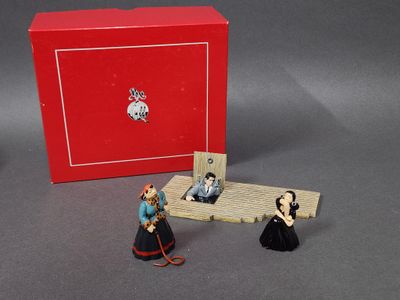 trois figurines représentant des personnes assises sur un banc devant une boîte rouge