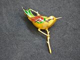 yellow bird broochle with green and red feathers sitting on a black surface
