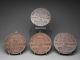 trois médailles de bronze portant des noms, exposées sur un fond gris