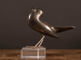 an image of a bronze bird on a clear base on a wooden table