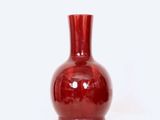 un vase rouge posé sur une surface blanche