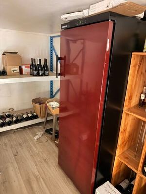 un réfrigérateur rouge au milieu d'une pièce, avec des bouteilles de vin sur les étagères