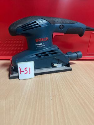 une ponceuse orbitale Bosch posée sur une table, à côté d'une boîte rouge
