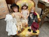 three dolls that are sitting on a yellow chair