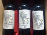 three bottles of red wine in a cardboard box on a table