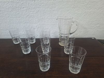 six verres et un pichet posés sur une table en bois