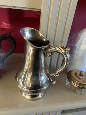 un pichet en argent posé sur une étagère à côté d'autres objets en argent