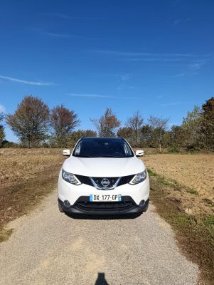 the front of a white nissan suv parked on a dirt road