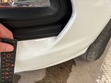 someone is measuring the front bumper of a white car with a ruler