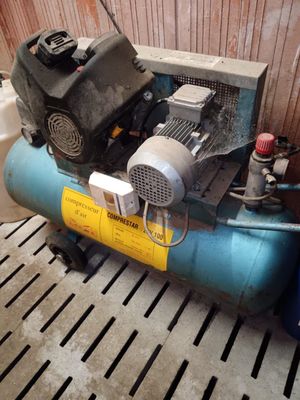 a blue air compressor sitting on the floor next to a tank