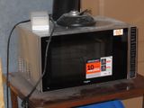 a microwave sitting on a table with a blue trash can in front of it